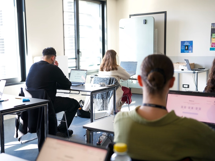 Des étudiants dans une salle de classe en train de passer des examens en ligne surveillés par un professeur